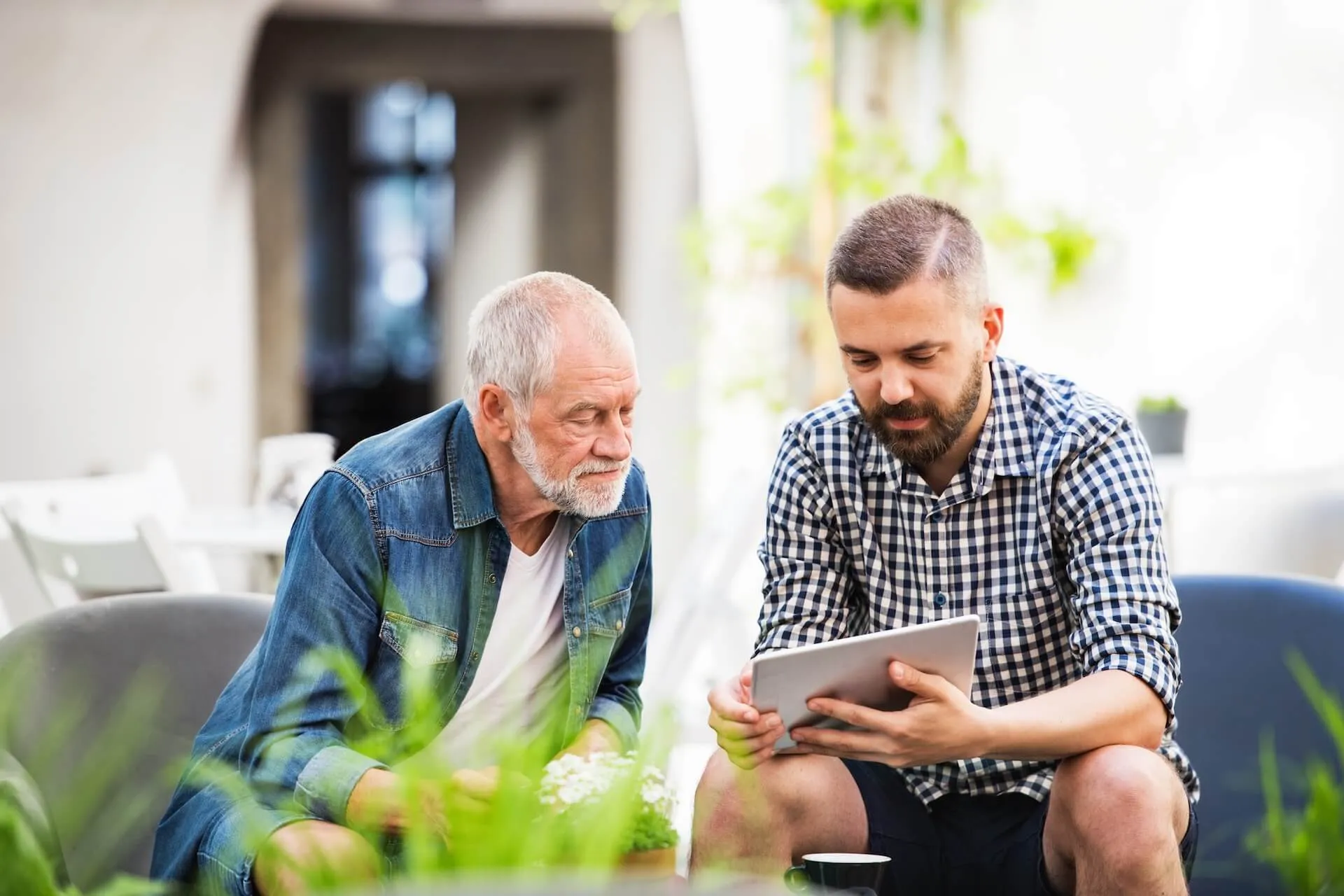 two men sitting on a couch looking at a tablet computer